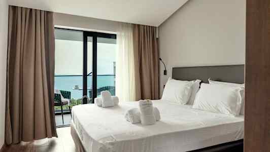 Ett hotellrum med en bäddad säng och utgång till en balkong med havsutsikt. (AI-genererad text)