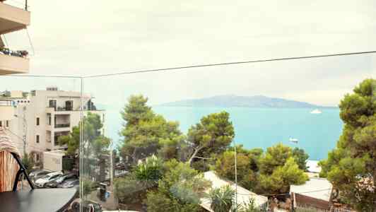 Vy från en balkong mot havet och grönskande träd. (AI-genererad text)