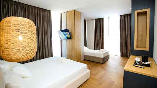 Ett hotellrum med två sängar, en hängande lampa, en väggmonterad TV och ett skrivbord med kaffekokare. (AI-genererad text)