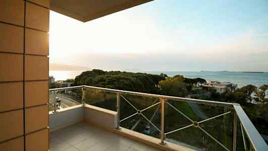 En balkong med glasräcke och utsikt över havet och grönområden. (AI-genererad text)