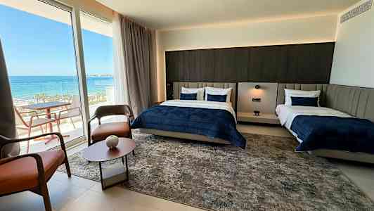 Ett hotellrum med två sängar och en balkong med havsutsikt. (AI-genererad text)