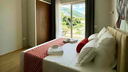 Ett hotellrum med en säng, dekorerad med röda kuddar och sängöverkast, samt utsikt mot ett grönskande landskap från fönstret. (AI-genererad text)