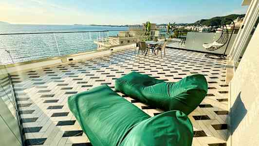 En terrass med havsutsikt, gröna sittsäckar, ett bord med stolar och en hängande stol. (AI-genererad text)