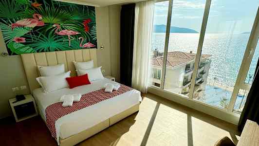 Sovrum med stor säng, flamingomotiv på väggen och havsutsikt genom panoramafönster. (AI-genererad text)