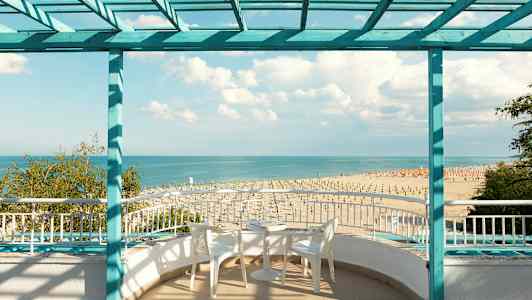 Utsikt mot stranden och havet från en terrass med sittmöbler. (AI-genererad text)