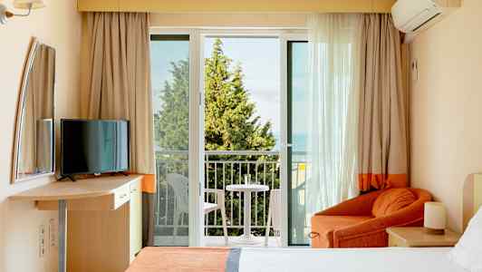 Ett hotellrum med balkong, säng, fåtölj och TV. (AI-genererad text)