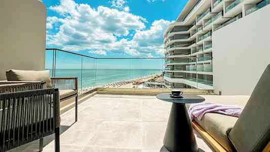 Utsikt från en terrass mot havet och en del av en byggnad med modern design. (AI-genererad text)