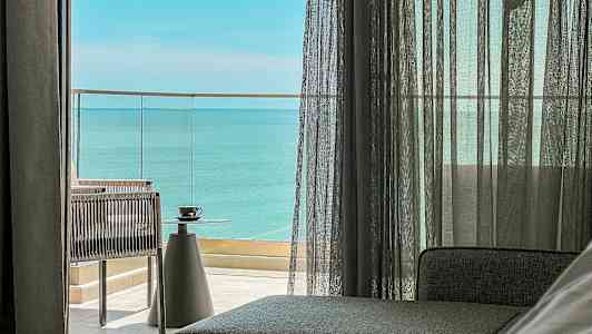 Utsikt från ett rum med glasdörrar som leder till en balkong med havsutsikt. En kopp står på ett bord. (AI-genererad text)