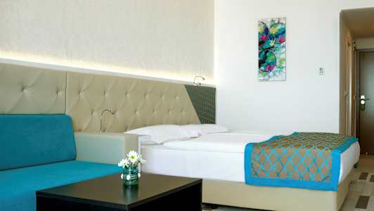 Ett modernt hotellrum med en dubbelsäng, turkos soffa och väggkonst. (AI-genererad text)