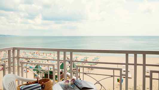 Utsikt från balkong mot en strand med parasoller och solstolar samt havet i bakgrunden. (AI-genererad text)