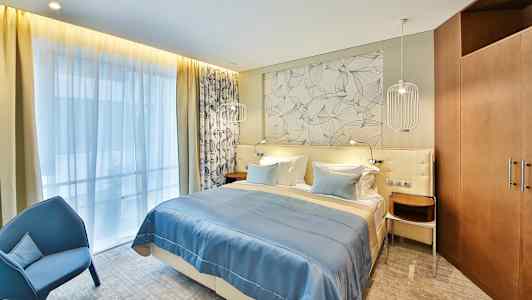 Ett hotellrum med en dubbelsäng, blått sängöverkast och dekorativ vägg bakom sängen. (AI-genererad text)