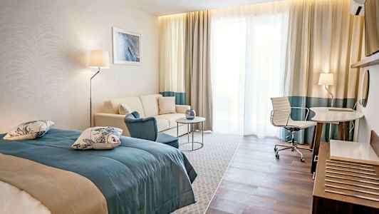 Ett hotellrum med en säng, soffa, bord och skrivbord med stol. (AI-genererad text)