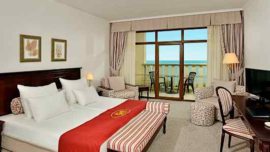 Ett hotellrum med dubbelsäng, sittgrupp, ett skrivbord och balkong med havsutsikt. (AI-genererad text)