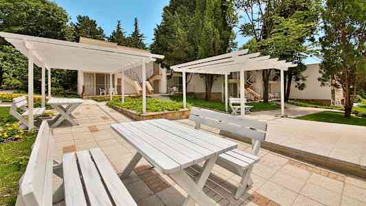 Vitmålade bord och bänkar utomhus omgivna av grönska. (AI-genererad text)