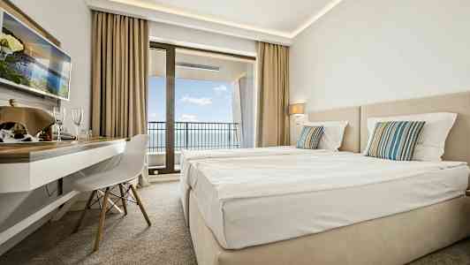 Hotellrum med två sängar, skrivbord och balkong med utsikt över havet. (AI-genererad text)