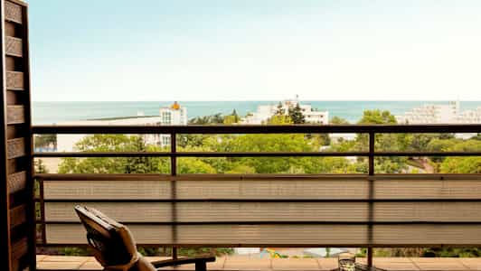 Utsikt från en balkong över grönska, byggnader och havet. (AI-genererad text)
