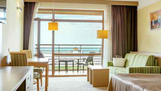 Ett hotellrum med sittområde, bord, säng och balkong med utsikt. (AI-genererad text)