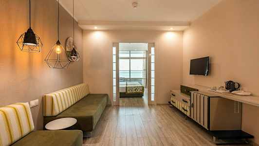 Ett hotellrum med en sittbänk, bord, TV och en säng i bakgrunden. (AI-genererad text)