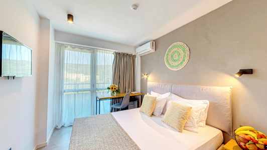 Ett hotellrum med en säng, ett skrivbord, en stol, en skål med frukt på ett nattduksbord och en balkong i bakgrunden. (AI-genererad text)