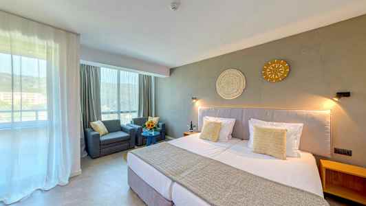 Ett hotellrum med en stor säng, två fåtöljer vid ett bord och dekoration på väggen. (AI-genererad text)