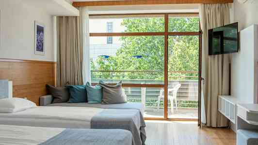 Ett hotellrum med två sängar, en soffa med färgglada kuddar och en glasdörr som leder till en balkong. (AI-genererad text)