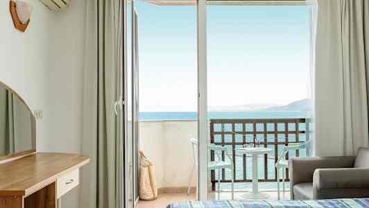 Hotelrum med öppen balkongdörr och havsutsikt. (AI-genererad text)