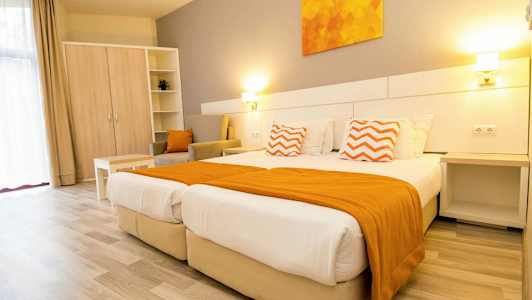 Ett ljust hotellrum med två sängar, orange detaljer och möbler. (AI-genererad text)