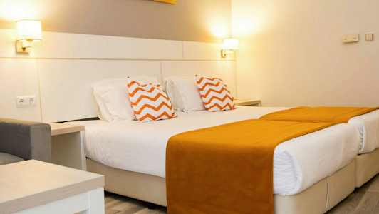 Ett hotellrum med två enkelsängar med orange sängöverdrag och prydnadskuddar med zigzag-mönster. (AI-genererad text)