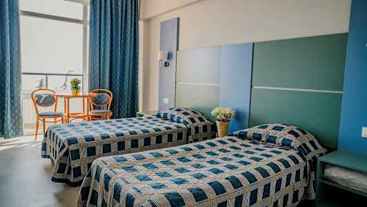 Två enkelsängar i ett rum med blå och grå inredning. Ett litet bord med två stolar står vid ett stort fönster. (AI-genererad text)