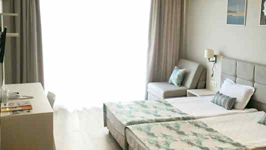 Ljust rum med två enkelsängar, en soffa och skrivbord. (AI-genererad text)