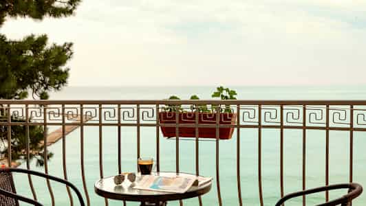 En balkong med utsikt över havet, med ett bord, stolar och en blomlåda. (AI-genererad text)