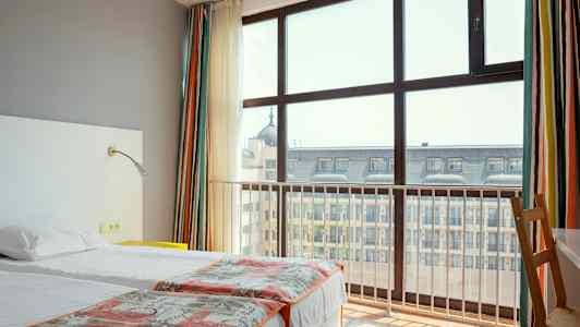 Hotellrum med två enkelsängar och stort fönster mot stadsvy. (AI-genererad text)