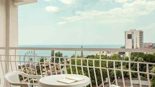 Utsikt från balkong med bord och två stolar, hav och städer i bakgrunden. (AI-genererad text)