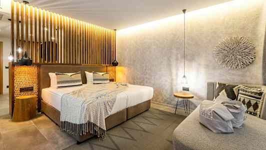 Sovrum med modern inredning, dubbelsäng med neutrala lakan och dekorativa kuddar, samt en soffa med en påse placerad ovanpå. (AI-genererad text)