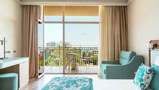 Hotellrum med dubbelsäng, turkos inredning och balkong med utsikt. (AI-genererad text)