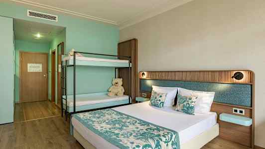 Ett hotellrum med en dubbelsäng och en våningssäng, inrett i turkosa och beige färger. (AI-genererad text)