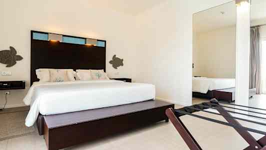 Ett hotellrum med en stor säng klädd i vita lakan och dekorativa kuddar, samt mörkt träpanel bakom sängen. (AI-genererad text)