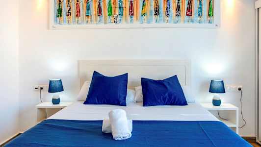 Bilden visar en säng med blåa kuddar och sängkläder, flankerad av två nattduksbord med blå lampor. (AI-genererad text)