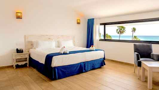 Ett hotellrum med en dubbelsäng och utsikt över havet genom ett stort fönster. (AI-genererad text)