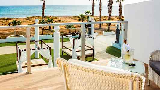 Utsikt från en balkong mot en grönskande trädgård med sängar under baldakiner och havet i bakgrunden. (AI-genererad text)