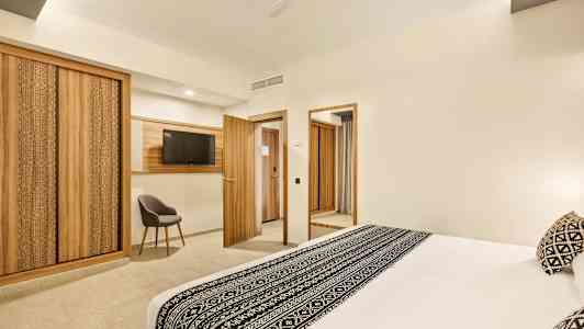 Ett hotellrum med en stor säng dekorerad med svartvitt mönster, trädetaljer i möbler och inredning inklusive garderober, dörrar och en TV-ram. (AI-genererad text)