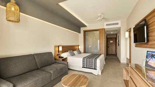 Ett modernt hotellrum med en säng, en soffa och ett bord. Det finns också en platt-TV på väggen. (AI-genererad text)