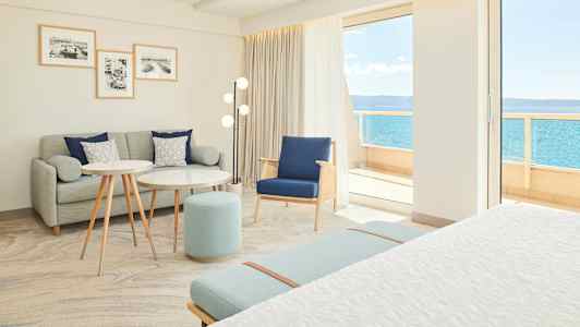 Ljust och modernt hotellrum med sittgrupp och utsikt mot havet. (AI-genererad text)