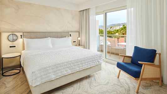 Sovrum med en stor säng och en blå stol nära glasdörrar till balkongen. (AI-genererad text)