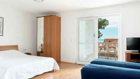 Ett hotellrum med säng, garderob, blå soffa, TV och balkong med utsikt. (AI-genererad text)