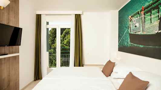 Ett hotellrum med en dubbelsäng, en vägg-TV och ett stort fönster med gröna gardiner. (AI-genererad text)