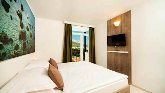 Ett hotellrum med en dubbelsäng, en väggdekoration, en väggmonterad TV och en balkong med utsikt. (AI-genererad text)