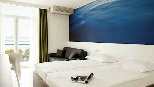 Dubbelrum med stor blå väggmålning bakom sängen. Balkong med havsutsikt. (AI-genererad text)