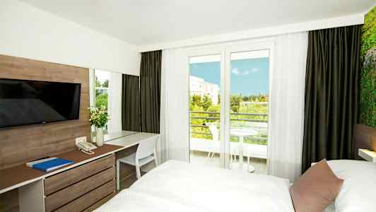 Hotellrum med två sängar, skrivbord, och en utsikt mot balkongen och grönska. (AI-genererad text)