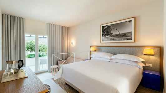 Sovrum med dubbelsäng, nattduksbord, tavla på väggen och balkong med utsikt. (AI-genererad text)